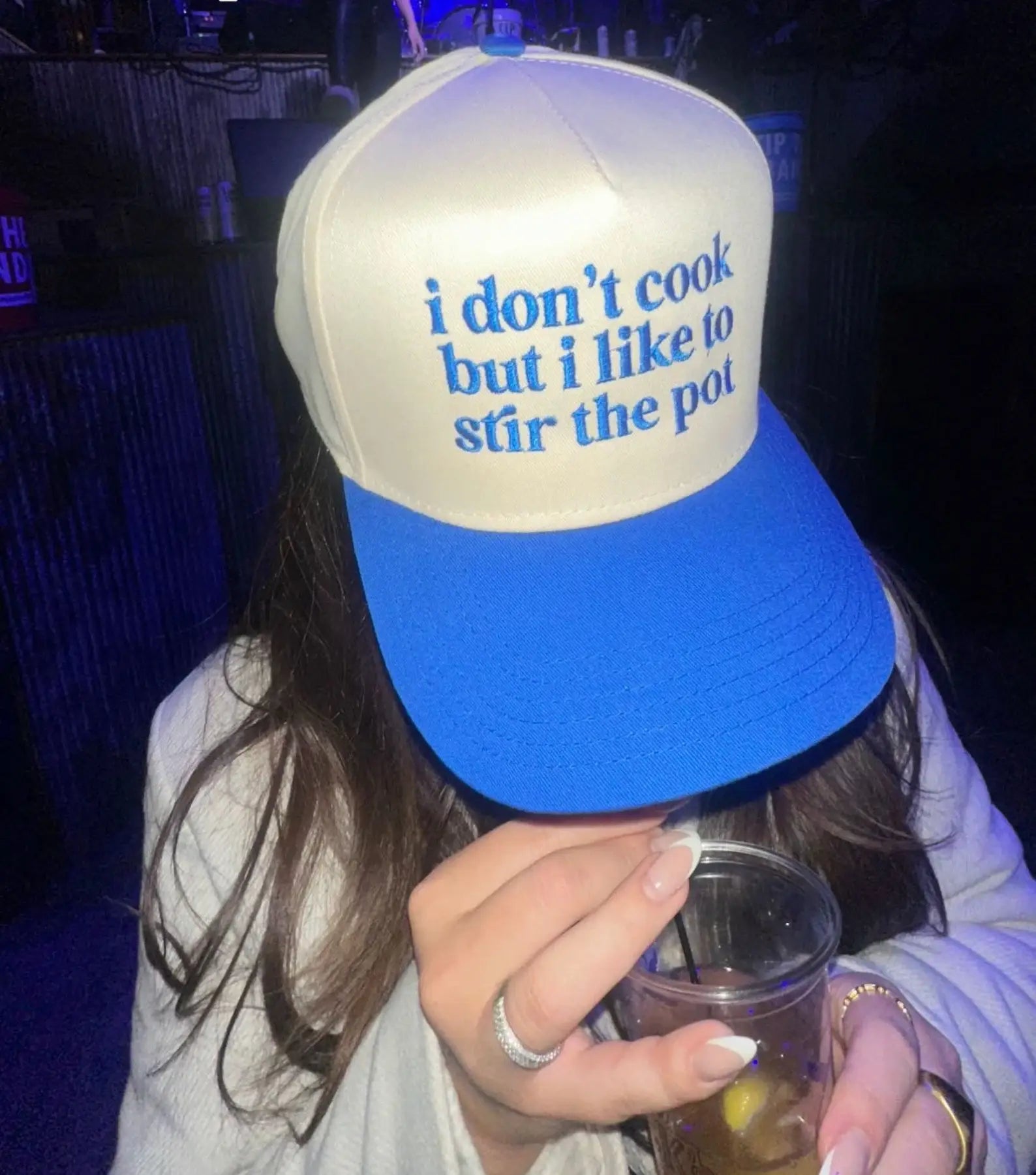 A person wearing a blue and white trucker hat with the text 'i don't cook but i like to stir the pot' embroidered on the front.