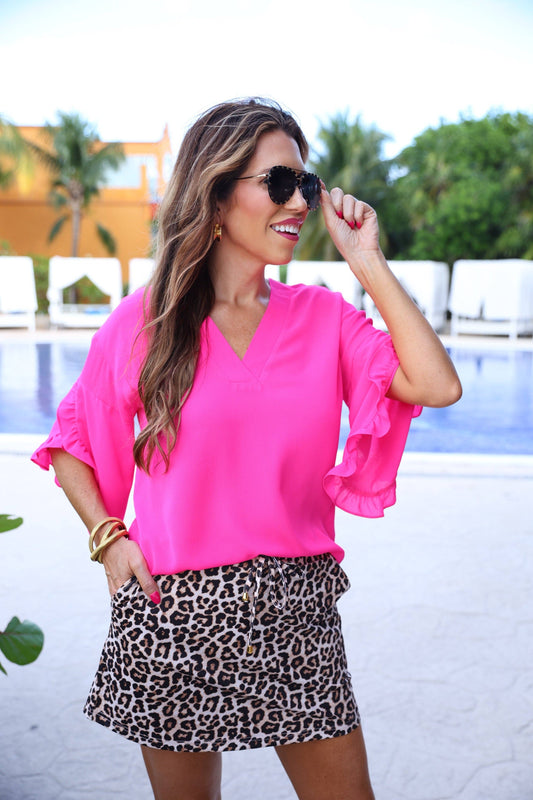 Woman wearing a bright pink blouse and leopard print skirt by a poolside.