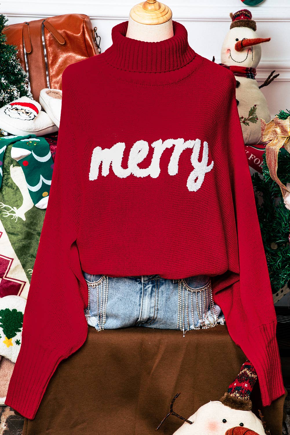 Red sweater with 'merry' text on a mannequin against a festive background
