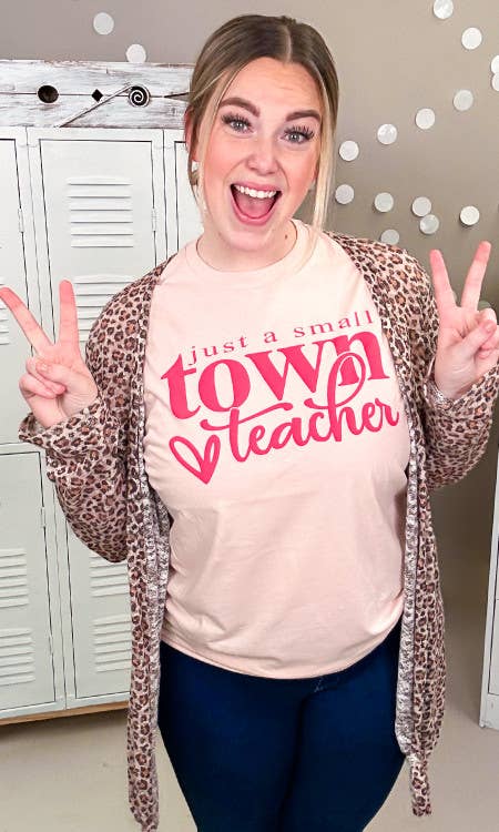 Person wearing a pink sweatshirt with 'Just a small town teacher' text, making peace signs.