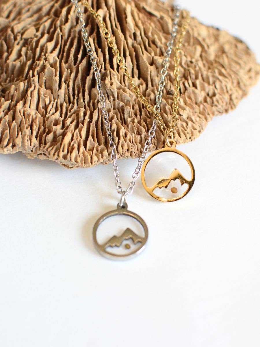 Two necklaces with scenic pendants on a textured surface