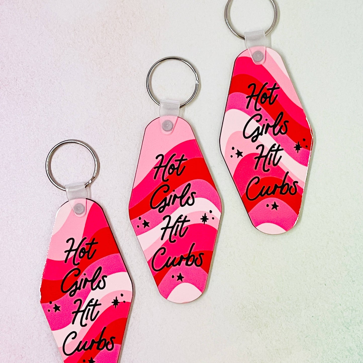  keychains with a double-sided design featuring text 'Hot Girls Hit Curbs' on a pink and red background.