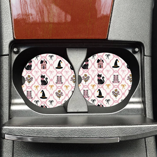 Two car coasters with a pink pattern featuring black cats, hats, and flowers in a black holder.
