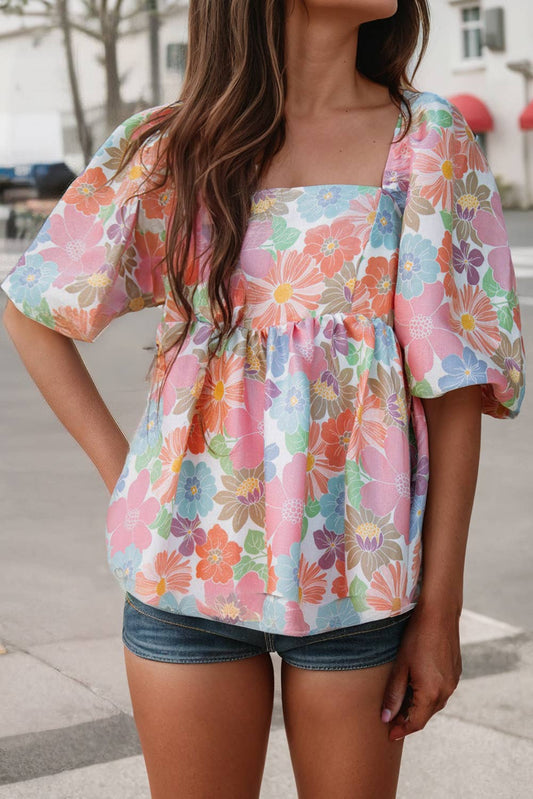 A woman wearing a multicolored floral puff sleeve square neck babydoll blouse with short denim shorts