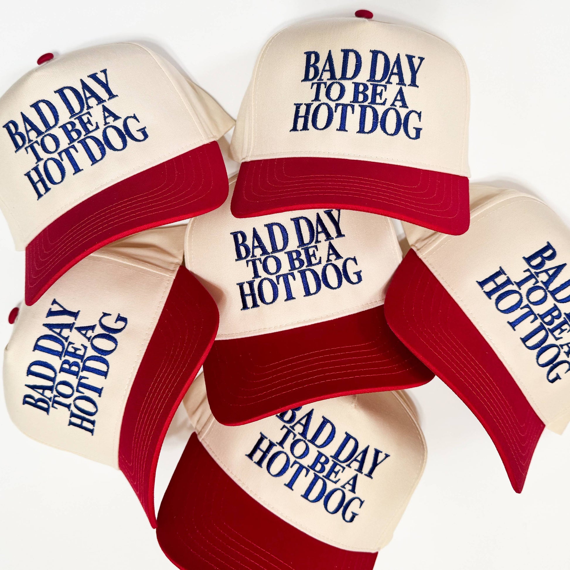 Beige caps with red brims and blue text 'Bad Day to be a Hotdog' on a white background