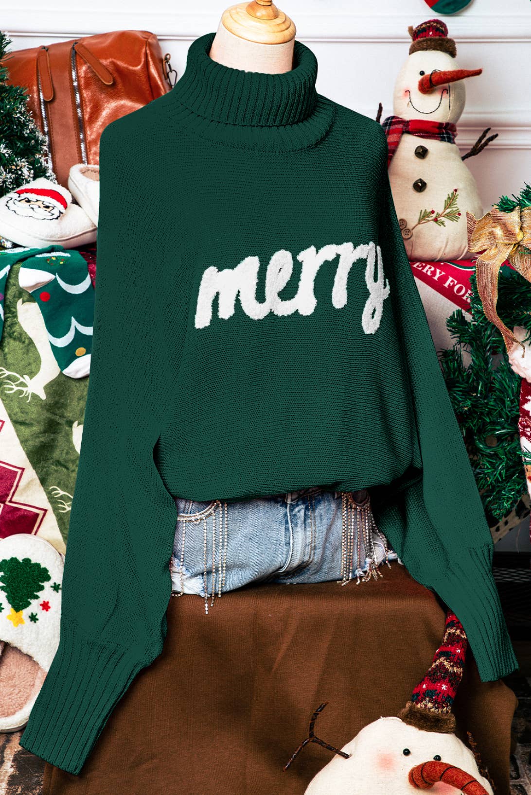 Green sweater with 'merry' text on a mannequin against a festive background