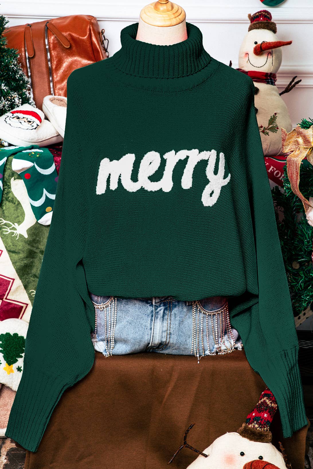 Green sweater with 'merry' text on a mannequin against a festive background