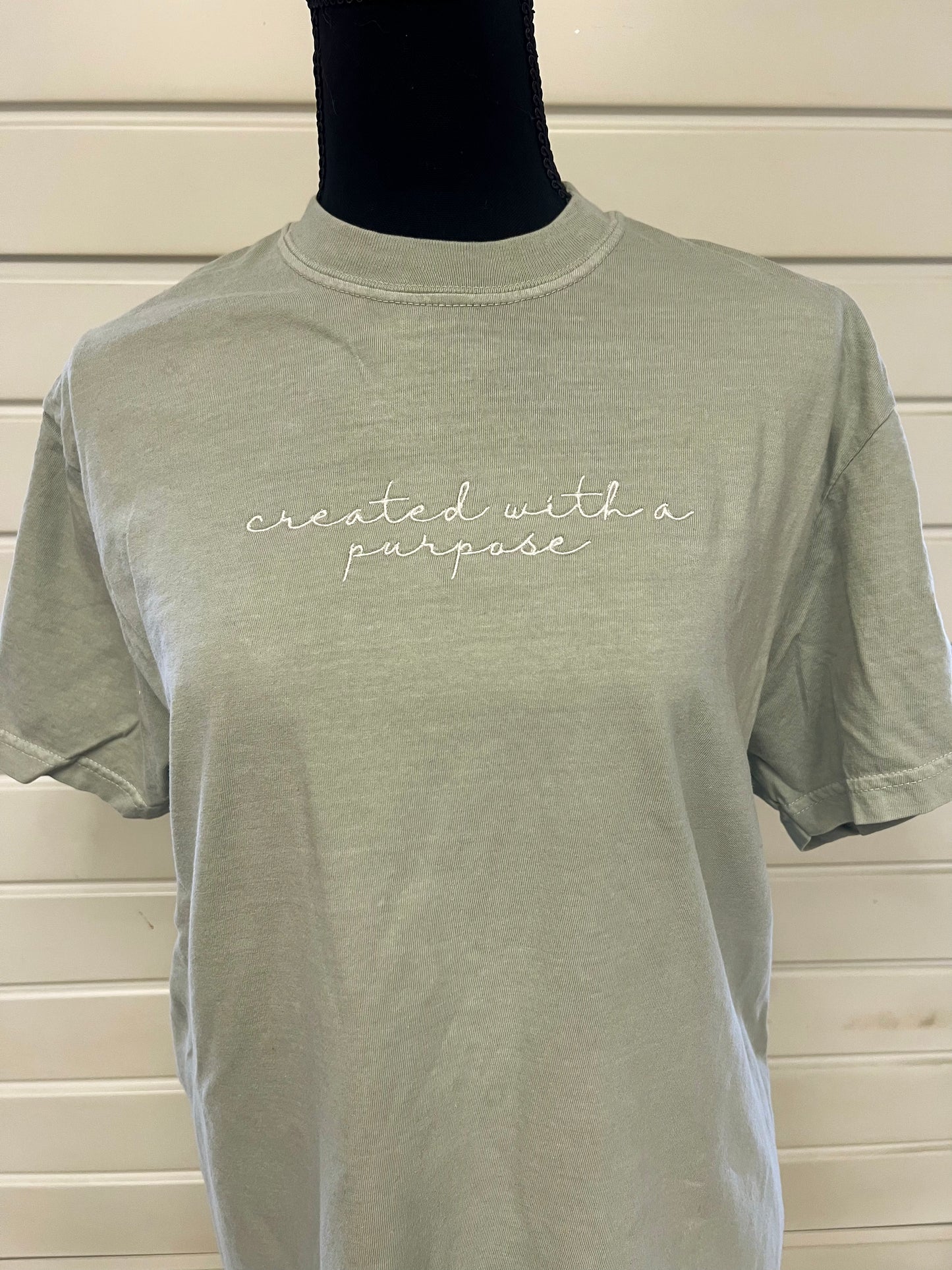 A green t-shirt with the phrase 'created with a purpose' embroidered in white on the front.