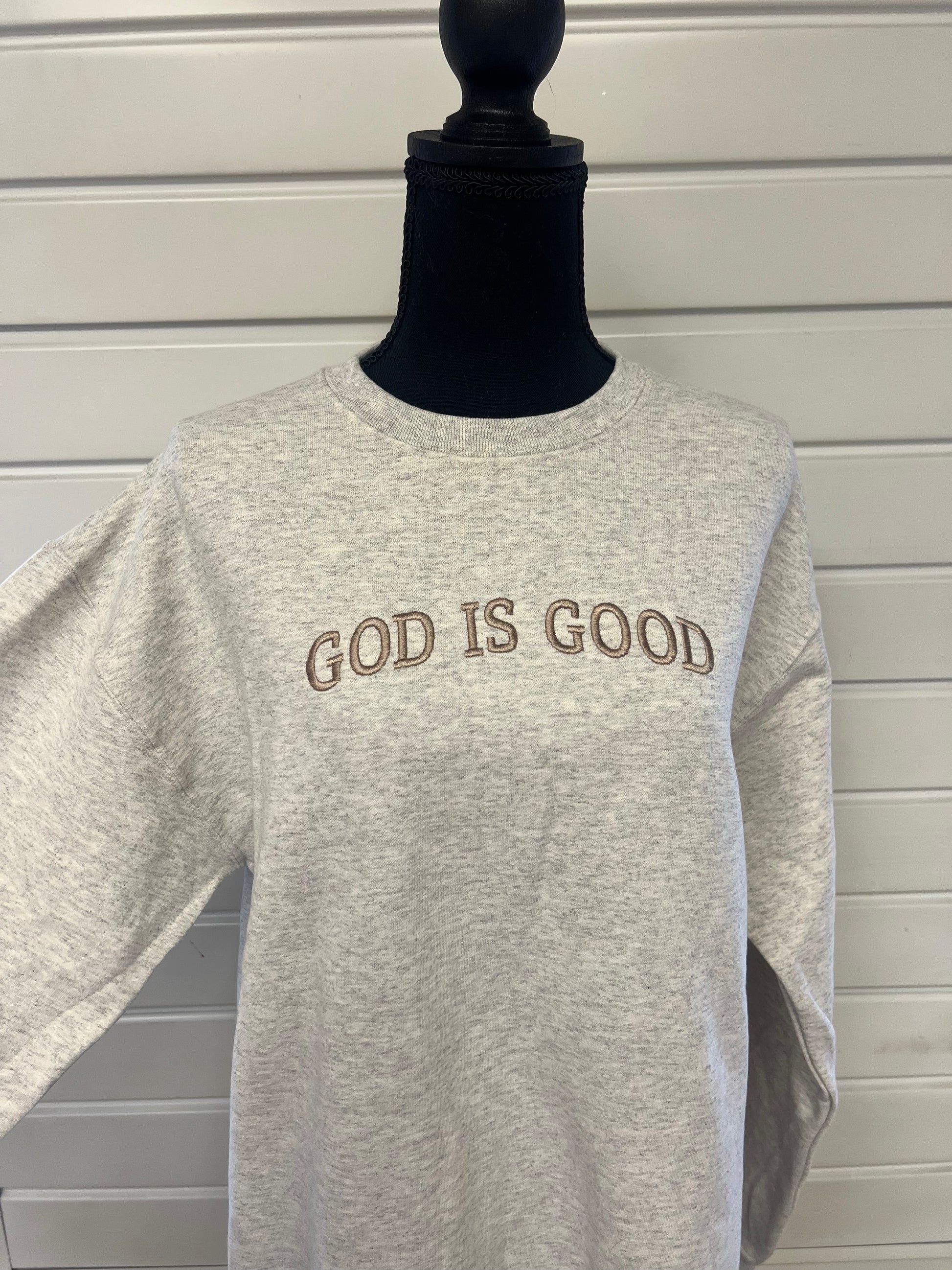 A gray sweatshirt with the phrase 'GOD IS GOOD' embroidered across the chest in capital letters.