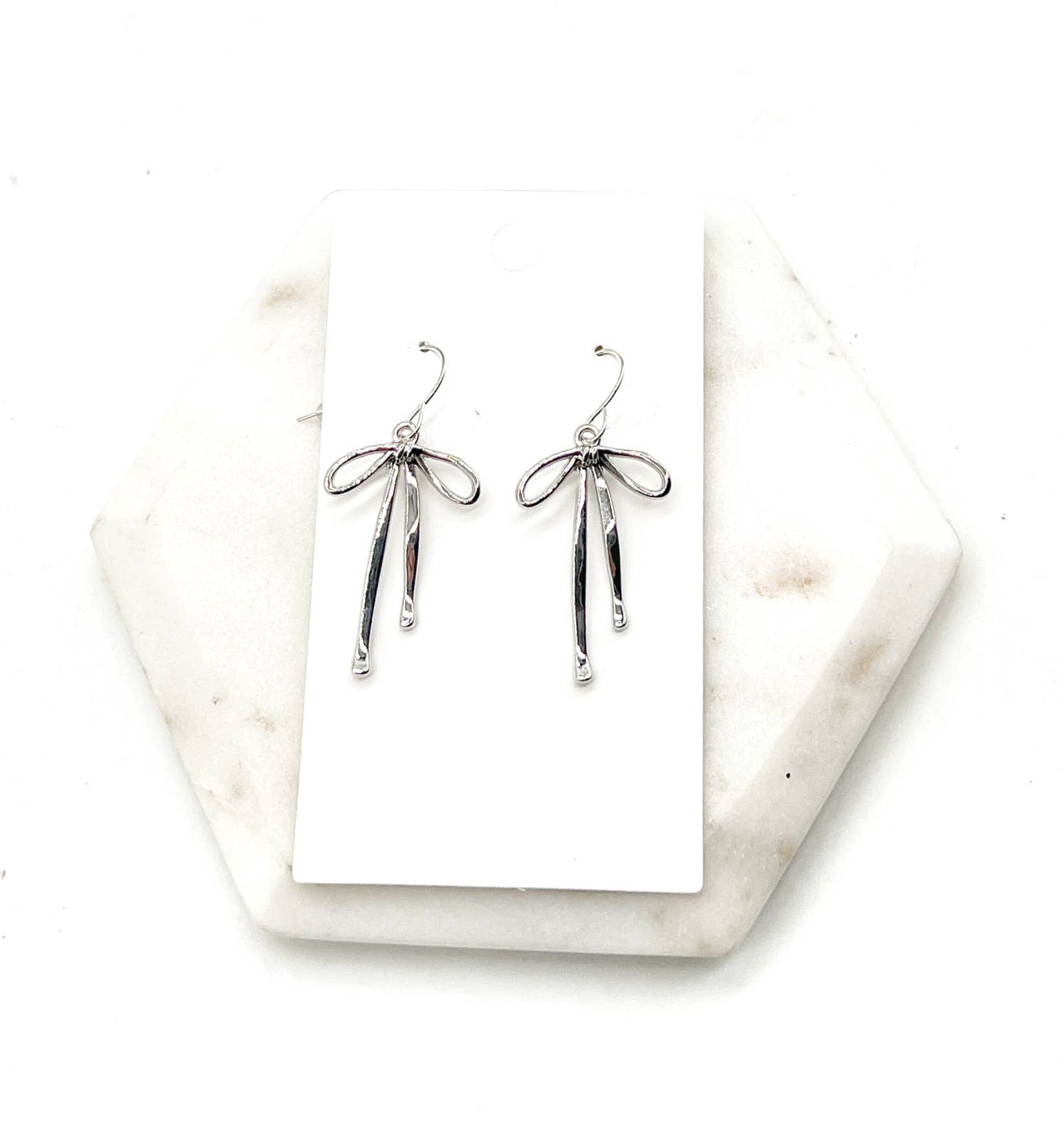 Silver bow-shaped earrings on a white card with a marble base