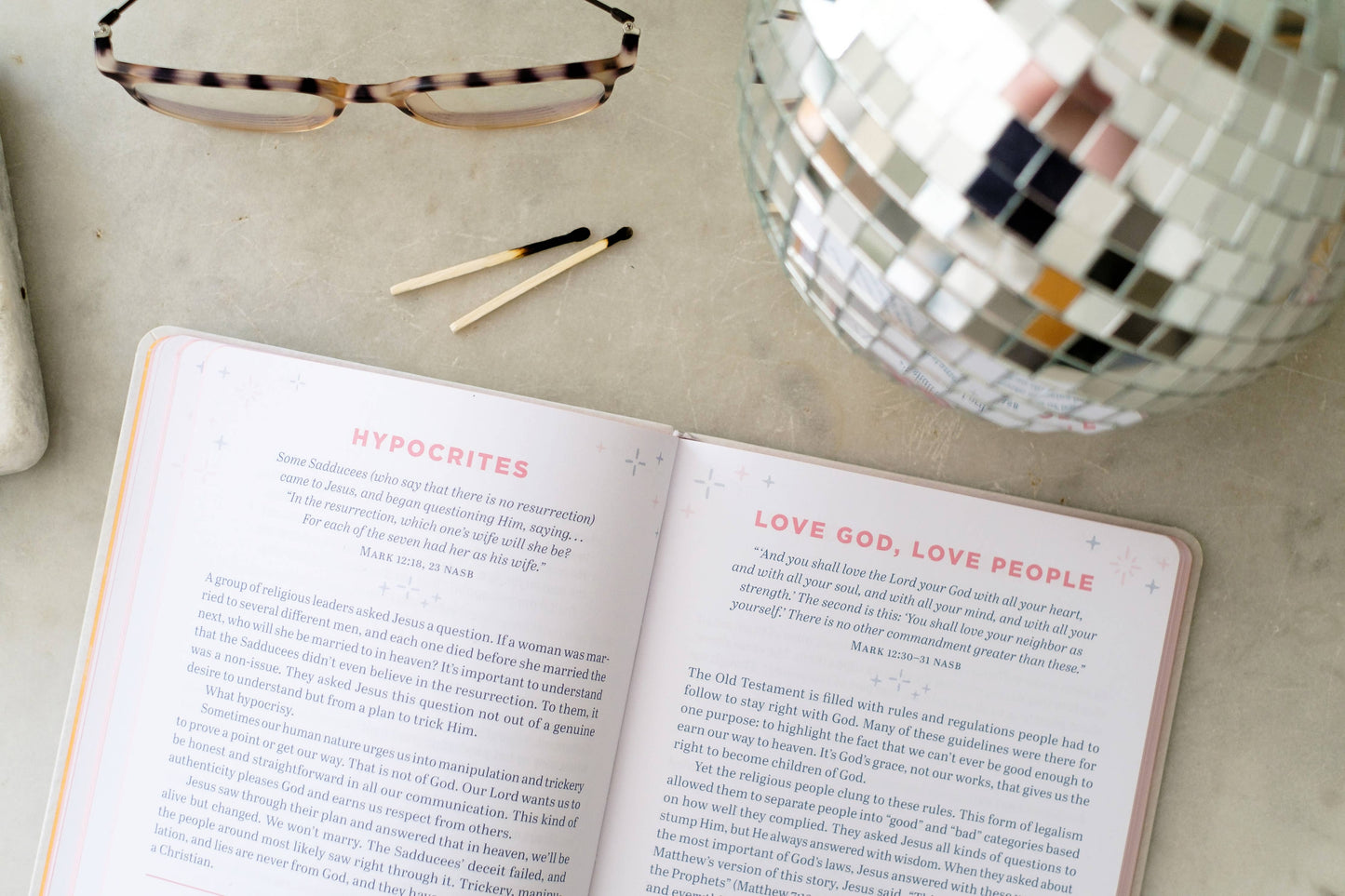 Open book on a surface with a disco ball and glasses in the background