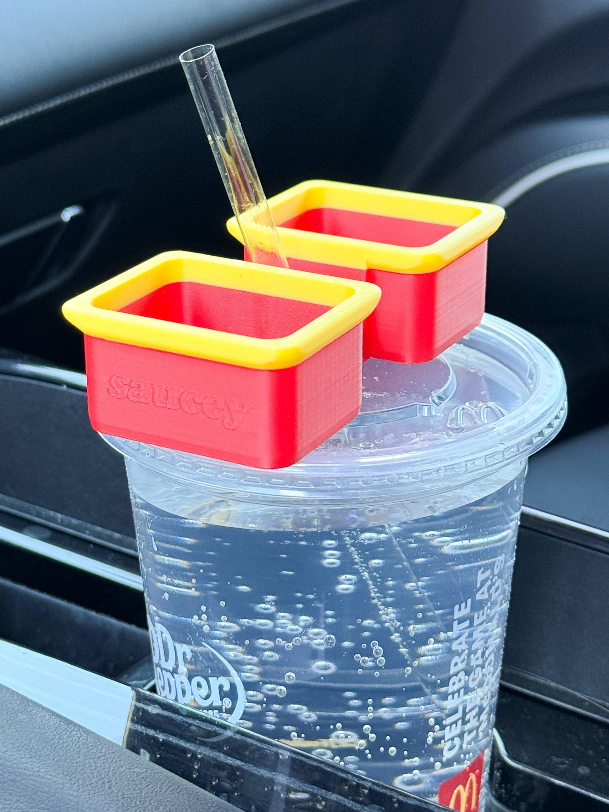 Two red and yellow McSaucey sauce holders attached to a clear straw cup, with one holding a red sauce dip and the other empty.