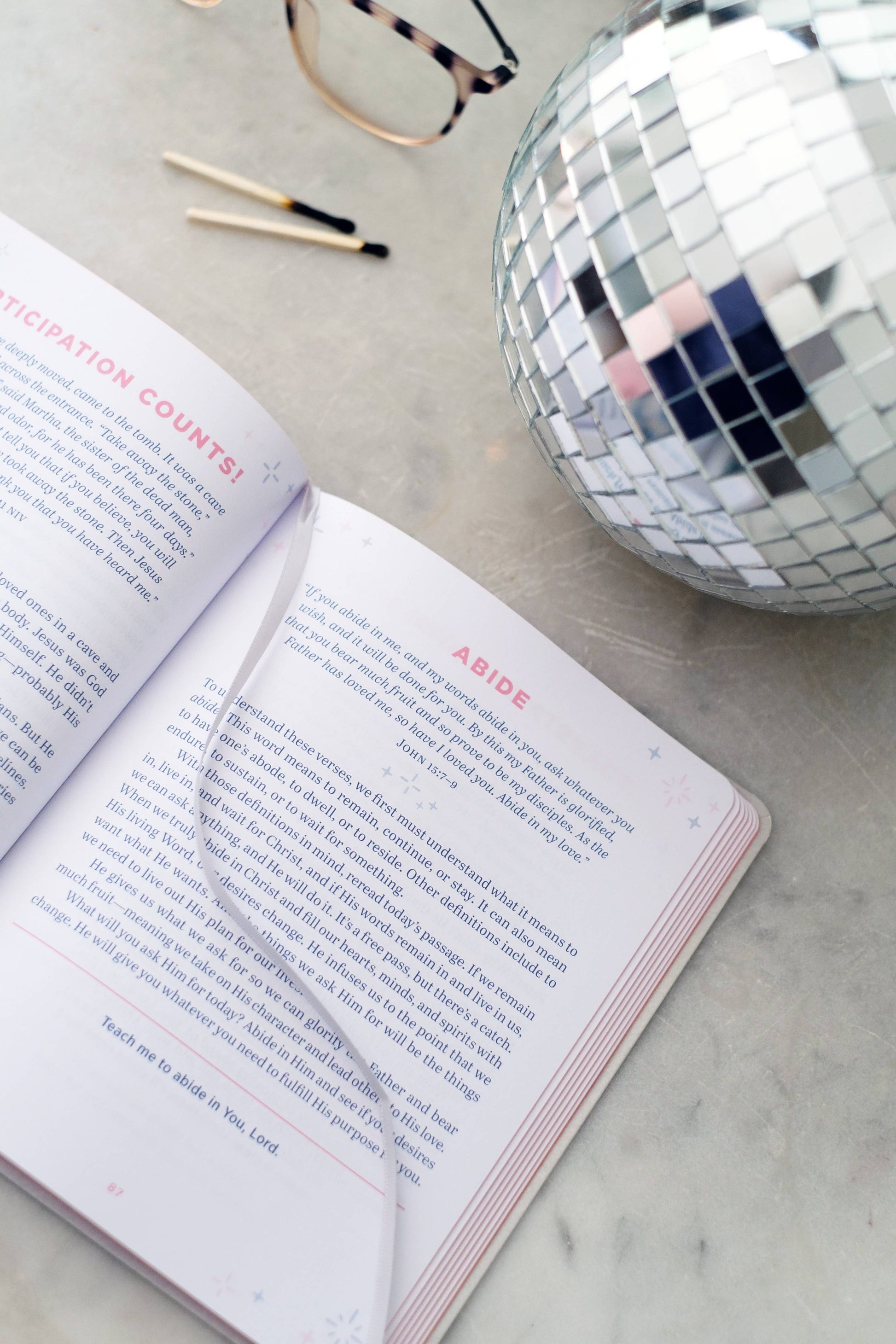 Open book on a marble surface with a disco ball and glasses in the background