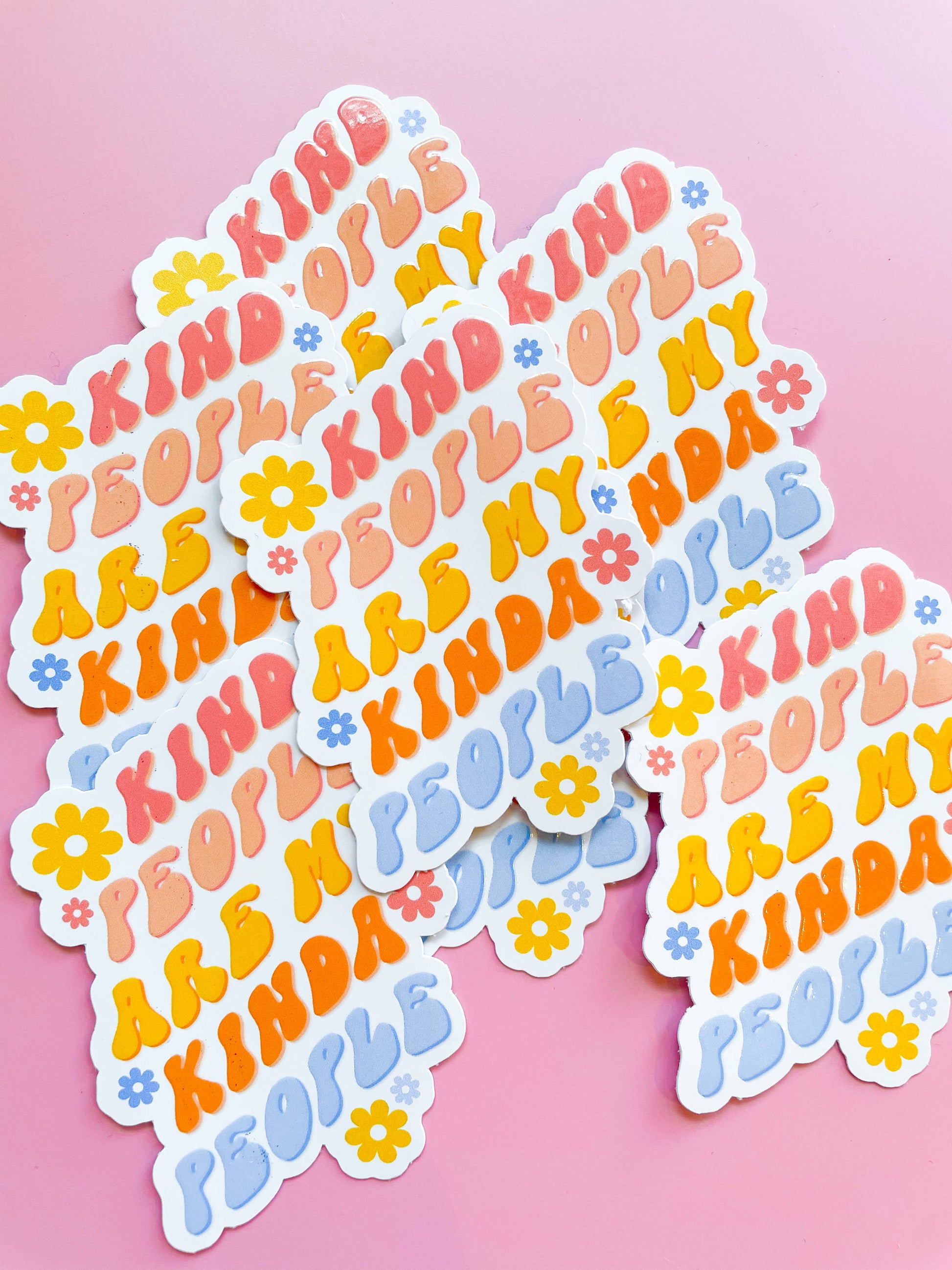 Stickers with the phrase 'Kind People are my Kinda People' printed in various colors, placed on a pink background.