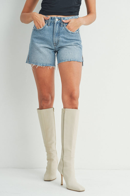 A pair of medium blue denim shorts with a side slit design, paired with beige knee-high boots.