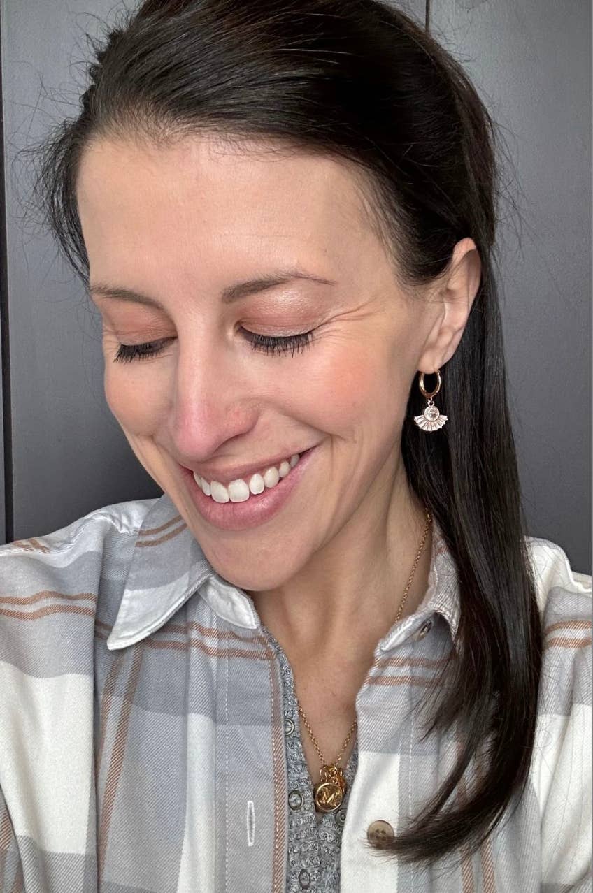 Woman with a smile, wearing a plaid shirt and gold earrings.