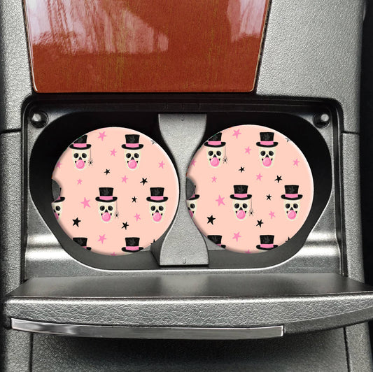 Two pink car coasters with black and white designs in a car cup holder.