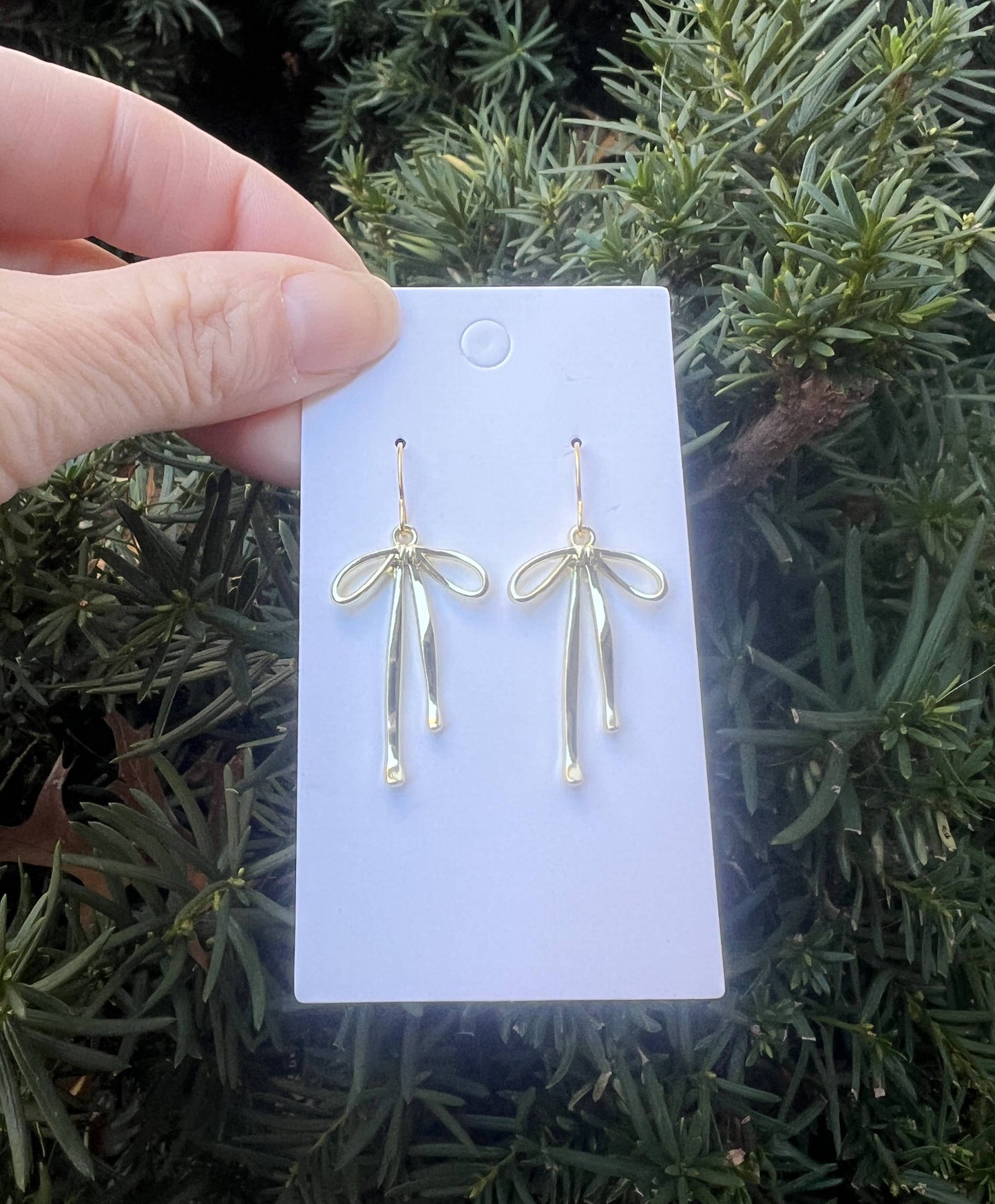 Gold earrings on a white card held by a hand with a green leafy background