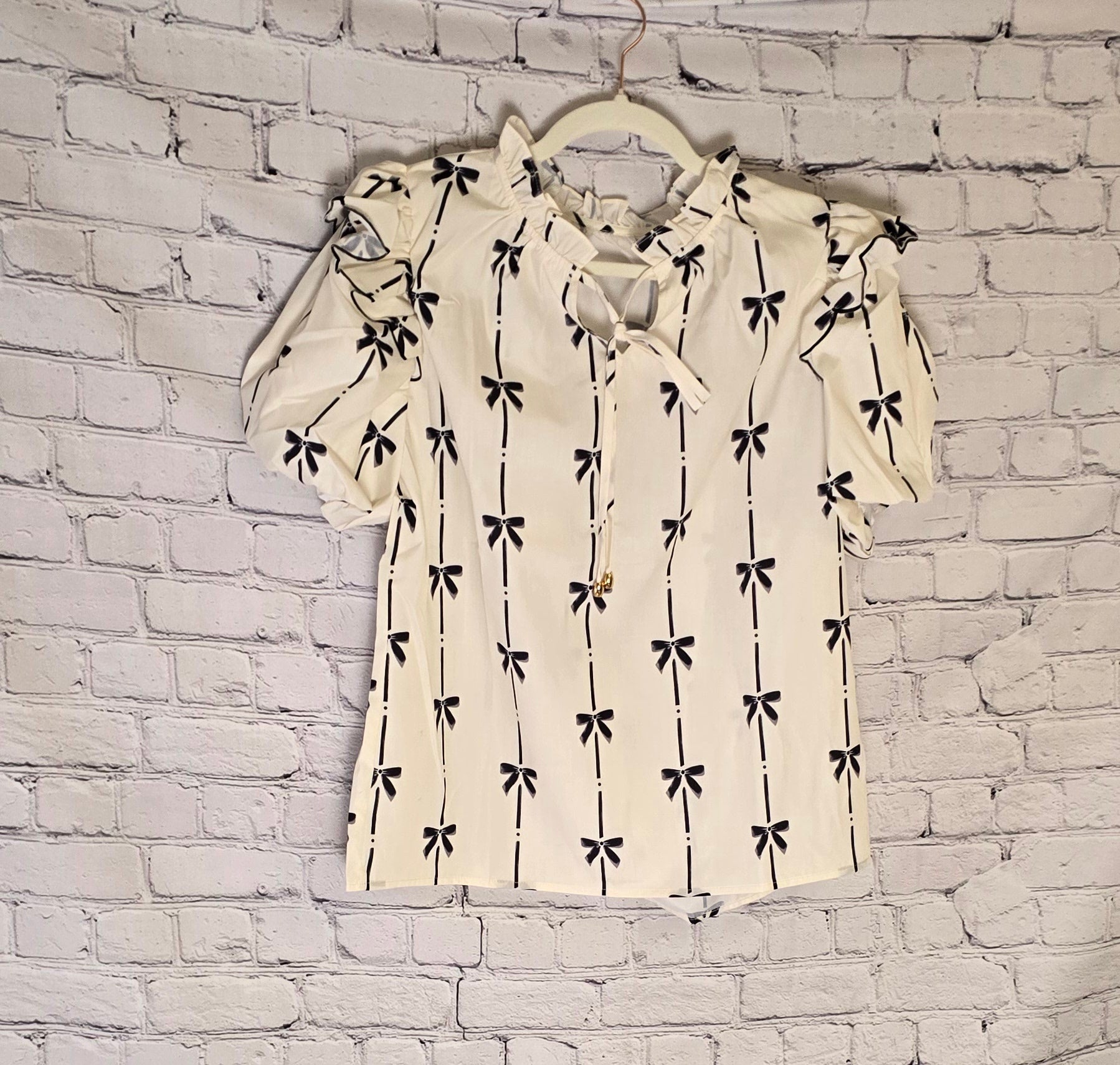 a white ruffled bubble sleeve notched neck blouse with a black pattern against a white wash brick wall
