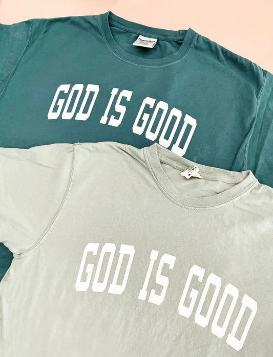 Two t shirts, one in sage green and another in dark Green laid over eachother stating God is Good