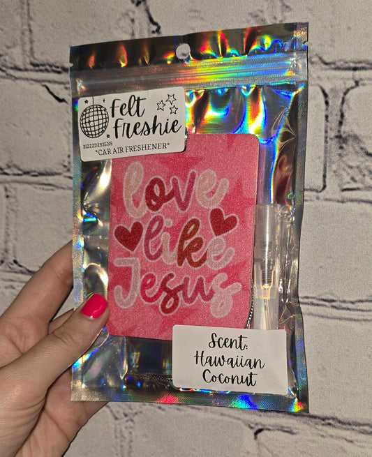 A hand holding a car freshener pack with 'Love Like Jesus' text and heart shapes, accompanied by a 3ml spray bottle.