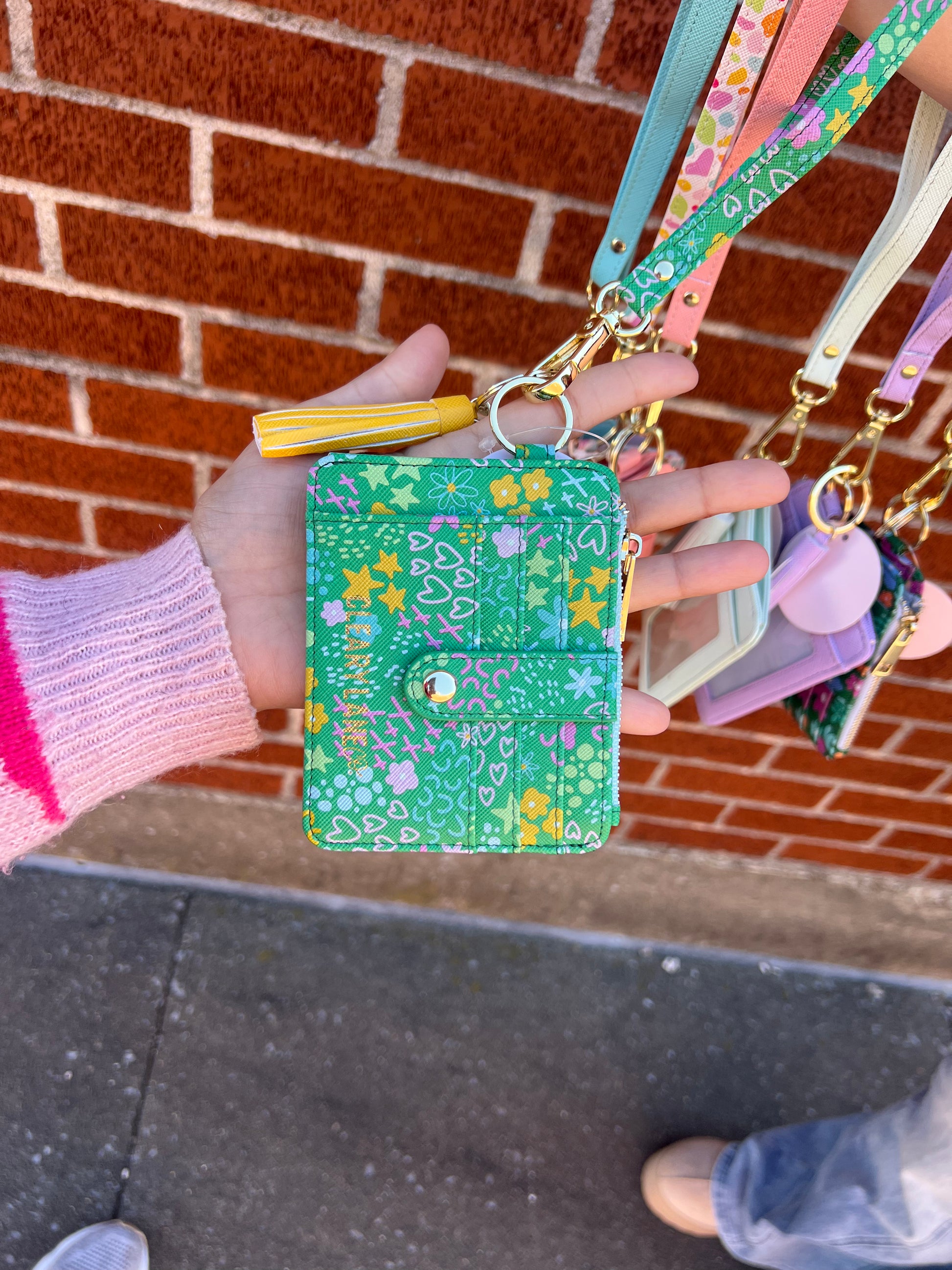 A green faux leather wallet keychain with a floral pattern being held by a person's hand, with a key ring and strap attached.